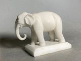 a white elephant statue on a marble base on a gray surface