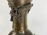 a brass vase with a bird on it on a table