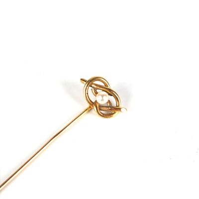 une broche en or sertie d'une perle, posée sur un fond blanc