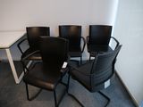 Trois chaises noires sont posées dans un coin, près d'une table blanche.