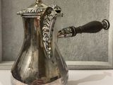 a silver coffee pot with a handle on a table