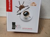 une boîte contenant une cafetière, posée par terre à côté d'un panneau