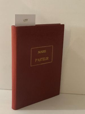 un livre rouge avec des lettres dorées posé sur une surface blanche