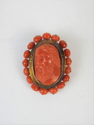 an image of a coral and gold broochle with a carved face on it