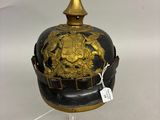 un casque ancien orné de décorations dorées, posé sur un socle transparent