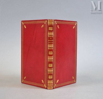 un livre rouge ouvert, aux bords dorés, posé sur une surface blanche