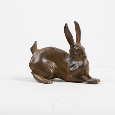 sculpture en bronze représentant un lapin couché sur une surface blanche