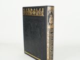 an old black book with gold trim sitting on top of a white surface