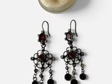 une paire de boucles d'oreilles noires et argentées ornées de grenats, accompagnée d'un bocal en verre