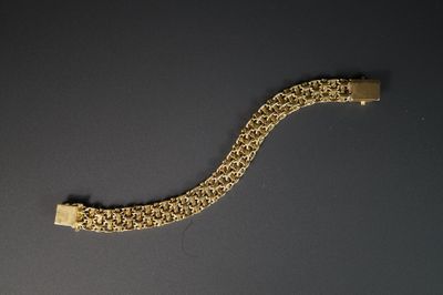 une image représentant un bracelet en or posé sur une surface noire
