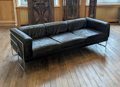 a black leather couch sitting on a wooden floor in a living room
