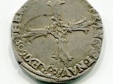 une vieille pièce d'argent ornée d'une croix, posée sur une surface blanche