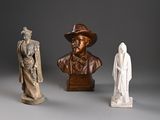 trois statues d'hommes coiffés de chapeaux et vêtus de capes, posées sur une surface grise