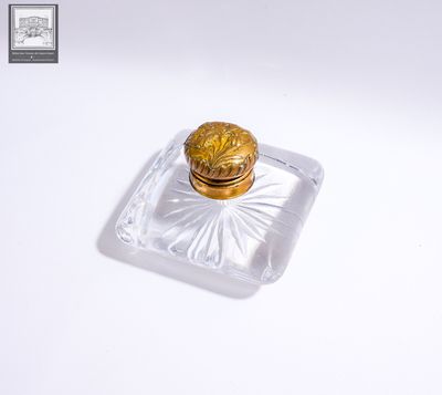 une petite boîte en verre avec un couvercle doré, posée sur une surface blanche