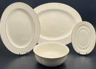 four pieces of white and gold dinnerware on a table