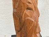 a wooden sculpture of a face on a black stand