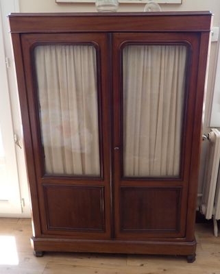 a wooden cabinet with two glass doors and a radiator in the corner