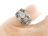 an image of a woman ' s hand holding a diamond and emerald ring