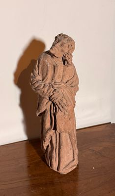 une statue représentant un homme tenant un enfant dans ses bras, posée sur un plancher en bois