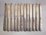 six couteaux anciens en métal argenté et un porte-couteaux posés sur une table