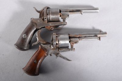deux vieux revolvers posés l'un sur l'autre sur une surface blanche