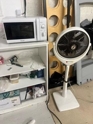 un ventilateur posé sur un support à côté d'un micro-ondes
