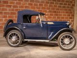 an old blue car parked in front of a brick wall