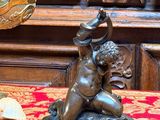 une statue en bronze représentant un garçon tenant un oiseau, posée sur une table