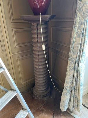 un grand vase rouge posé sur un socle à côté d'une échelle