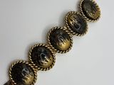 a close up of a gold and black bracelet on a white surface