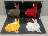 four different colored plastic rabbits on display in a glass case