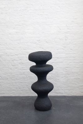 des pierres noires empilées les unes sur les autres devant un mur de briques blanches