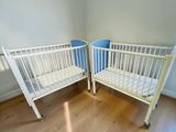 deux lits bébé dans un coin d'une pièce au sol en parquet