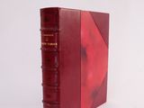 an old red book sitting on top of a white surface