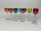 six verres à vin de différentes couleurs sont alignés sur une surface blanche