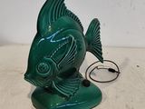 une statue de poisson verte posée sur une table, à côté d'un cordon