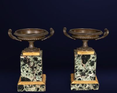 pair of bronze and marble urns on pedestals on a blue background