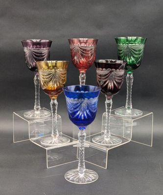 six verres à pied de couleurs différentes sont posés sur un socle transparent