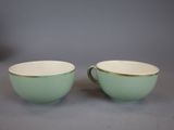 two green and white cups with gold rims on a gray surface