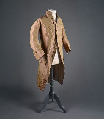 un vieux manteau posé sur un mannequin, devant un fond gris