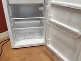 un petit réfrigérateur blanc dont la porte est ouverte, posé à même le sol