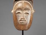 a wooden mask on a stand with a gray background