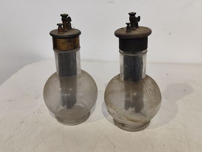une paire de bouteilles en verre anciennes avec des bouchons en métal, posées sur une table blanche