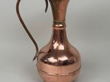 an antique copper pitcher with a curved handle on a white background