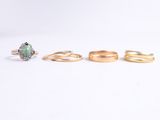 three gold rings and a green stone ring on a white background