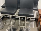 trois tabourets de bar en cuir noir posés sur un sol métallique