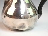 a silver pitcher with a black handle on a white table