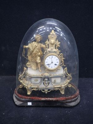 une horloge dorée sous un dôme en verre, posée sur une surface noire