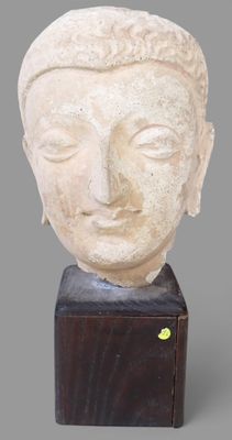 une photo représentant une statue représentant une tête posée sur un socle en bois