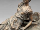 a bronze statue of a woman sitting on a vase